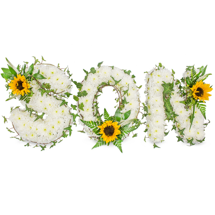 This meticulously constructed floral tribute spells the word SON in strong capital letters, set against a stark white background to highlight form and texture. Each letter is carefully built from hundreds of small, immaculate white chrysanthemums whose clustered blooms create a plush, almost quilted surface; the close packing of the petals produces soft relief and a peaceful, muted white tone. Interlaced throughout the chrysanthemum foundation are lengths of dark green ivy, their distinctive leaves winding in and out to trace the contours and soften the transitions between curves and angles. Lighter green fern fronds and assorted leafy sprigs are inserted to introduce depth and a variety of leaf textures, creating pockets of shadow and life within the letters. Three vivid sunflowers serve as intentional focal points: one rests on the upper-left curve of the S, another anchors the lower arc of the O amid fern greenery, and the third crowns the upper-right of the N; their bright yellow petals and rich brown centres provide contrast and a sense of warmth that counters the solemn white base. The overall composition reads as a respectful funeral tribute for a beloved son, photographed with clear, even lighting so that the tactile quality of the chrysanthemums, the glossy ivy, and the sunflower faces are all plainly visible. As a local arrangement often chosen by families in Orpington and visitors from nearby Goddington Park, it communicates calm, remembrance and a quiet celebration of life.